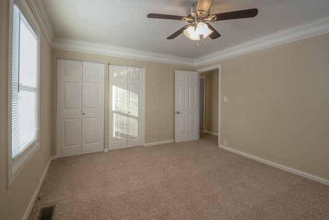 unfurnished bedroom with visible vents, light carpet, two closets, crown molding, and baseboards