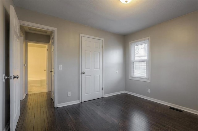 unfurnished bedroom featuring dark wood-style floors, visible vents, and baseboards