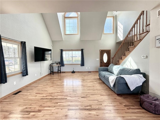 living area featuring visible vents, light wood-style floors, a high ceiling, and stairway