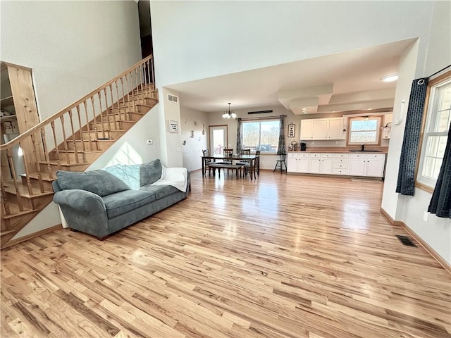 living area with stairs, visible vents, baseboards, and light wood-type flooring