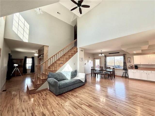 living area with visible vents, light wood-style floors, stairway, and ceiling fan with notable chandelier