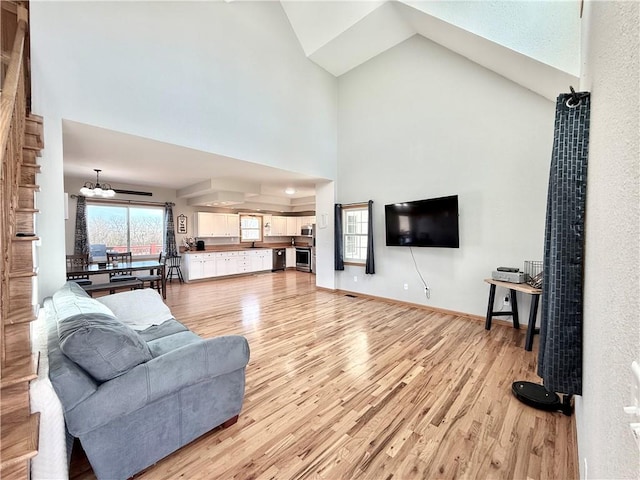 living room with light wood-style flooring, baseboards, and high vaulted ceiling