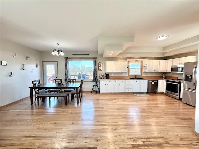 kitchen with a sink, white cabinetry, stainless steel appliances, light wood-style floors, and an inviting chandelier