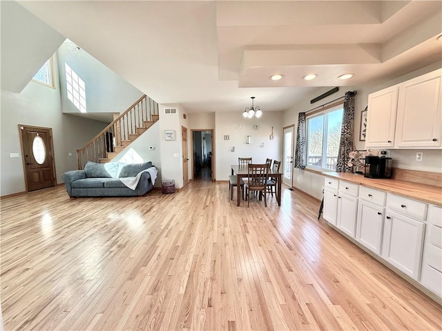 interior space featuring stairway, visible vents, light wood finished floors, a towering ceiling, and a chandelier