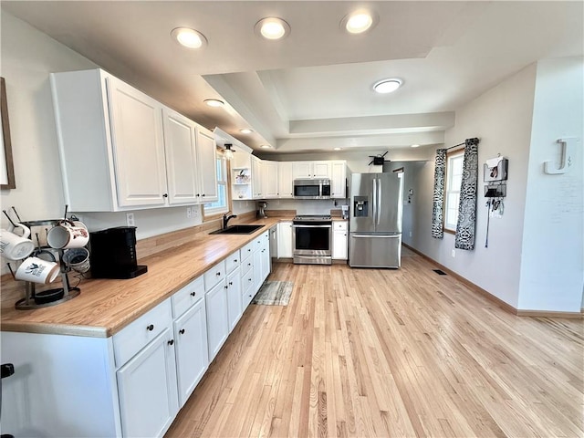 kitchen featuring a sink, stainless steel appliances, light wood-style flooring, and white cabinetry