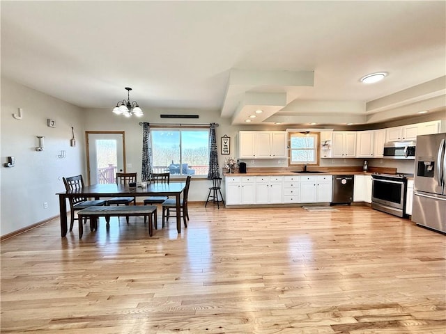 kitchen with light wood finished floors, a sink, stainless steel appliances, white cabinets, and a chandelier