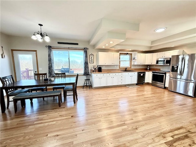 kitchen featuring light wood finished floors, a chandelier, white cabinets, stainless steel appliances, and a sink