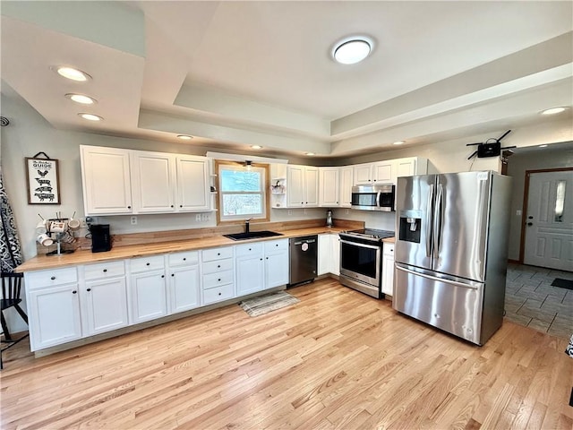 kitchen featuring a sink, wood counters, appliances with stainless steel finishes, and a tray ceiling