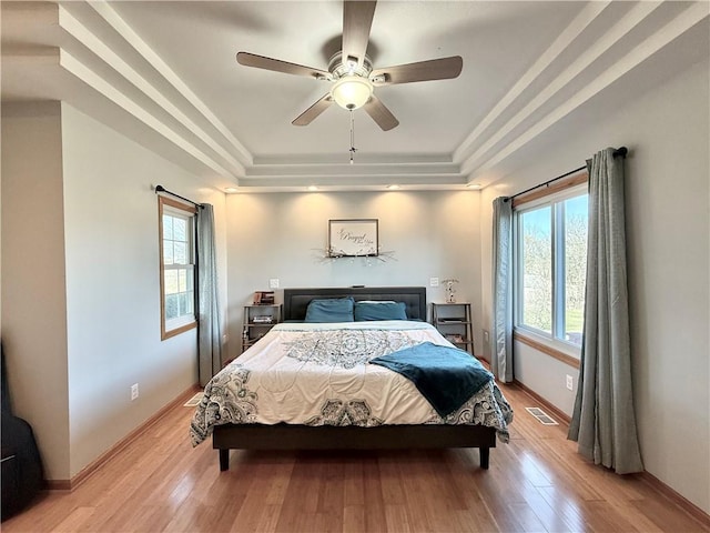 bedroom featuring a tray ceiling, multiple windows, and light wood-style floors