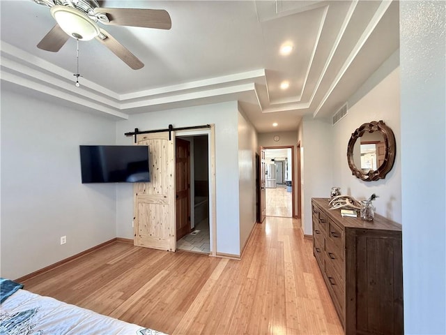 bedroom featuring visible vents, a barn door, baseboards, light wood finished floors, and a raised ceiling