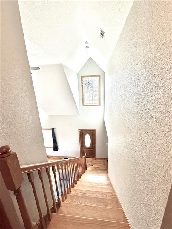 stairway with wood finished floors, a textured wall, visible vents, and vaulted ceiling