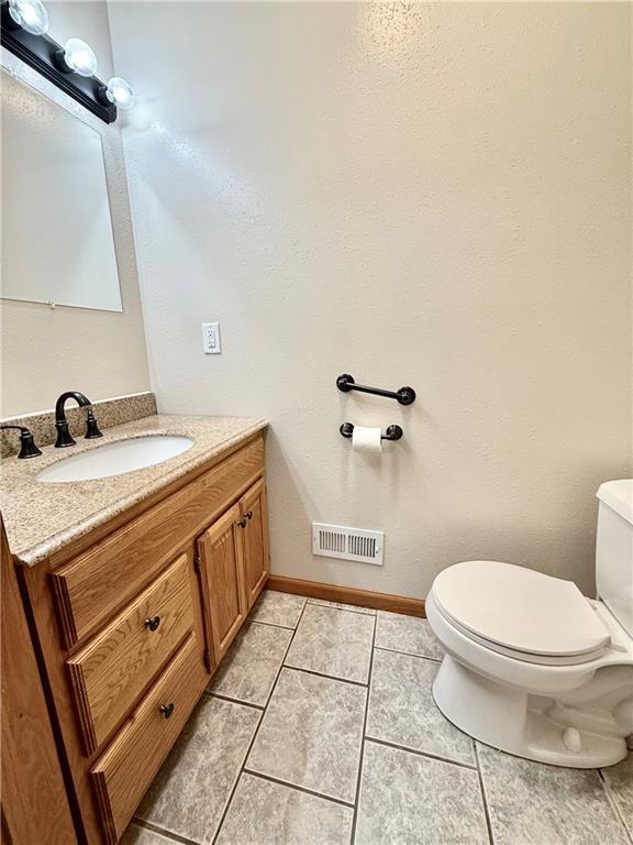 half bathroom with visible vents, baseboards, toilet, tile patterned floors, and vanity