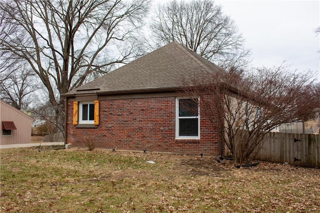 view of property exterior with brick siding, a lawn, a shingled roof, and fence