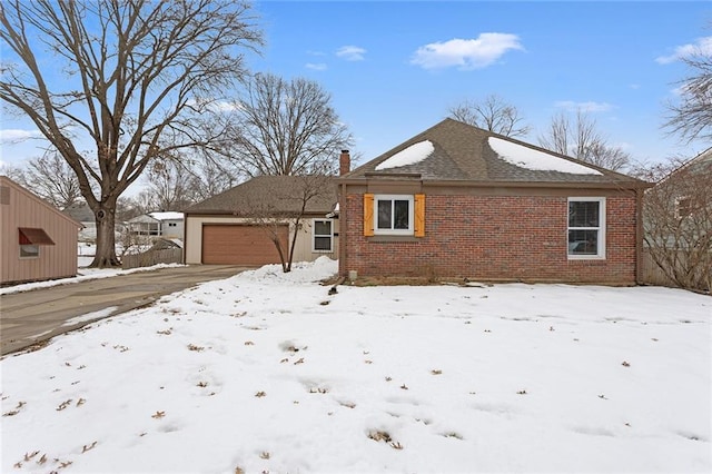 snow covered back of property with brick siding, an attached garage, and a chimney