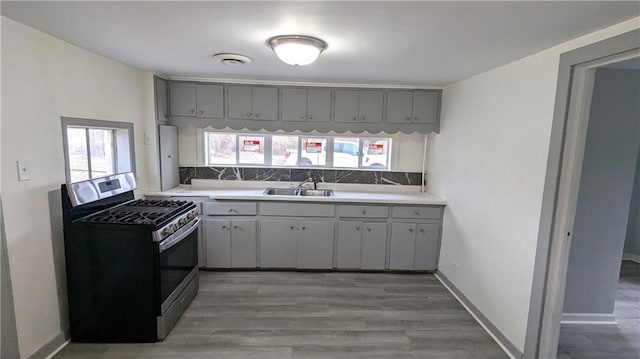 kitchen with a sink, gray cabinetry, stainless steel range with gas stovetop, and light countertops