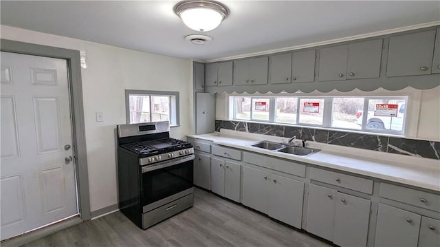 kitchen featuring backsplash, gray cabinets, wood finished floors, stainless steel gas stove, and a sink