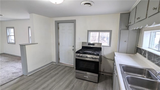 kitchen featuring stainless steel range with gas cooktop, decorative backsplash, light wood-style flooring, gray cabinets, and a sink