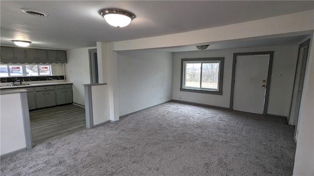 interior space with a sink, baseboards, visible vents, and light carpet