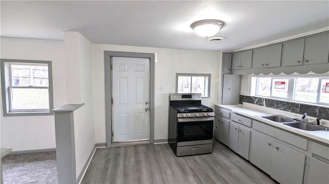 kitchen with gray cabinets, a sink, decorative backsplash, light wood-style floors, and stainless steel gas range oven