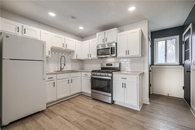 kitchen featuring light countertops, light wood-style flooring, white cabinets, stainless steel appliances, and a sink