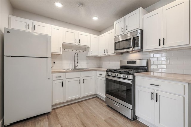 kitchen with light wood-style flooring, a sink, light countertops, appliances with stainless steel finishes, and white cabinetry