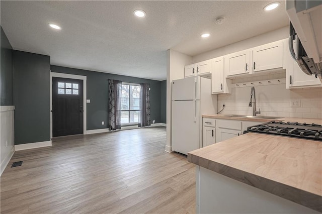 kitchen with a sink, backsplash, white cabinets, and freestanding refrigerator