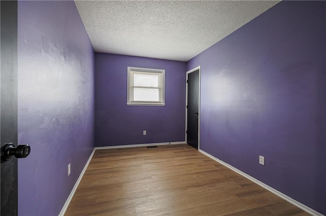 empty room with a textured ceiling, baseboards, and wood finished floors