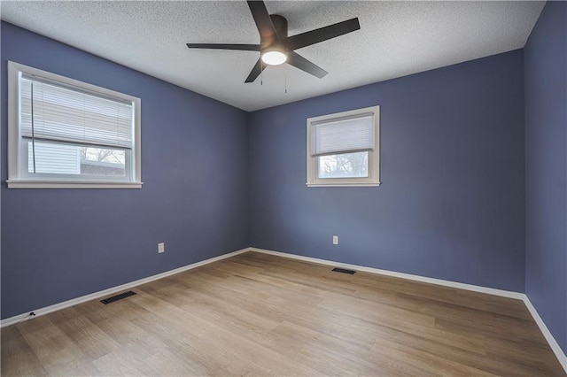 spare room featuring baseboards, plenty of natural light, a textured ceiling, and wood finished floors