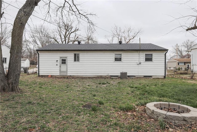 rear view of house with a lawn, central AC unit, an outdoor fire pit, and fence