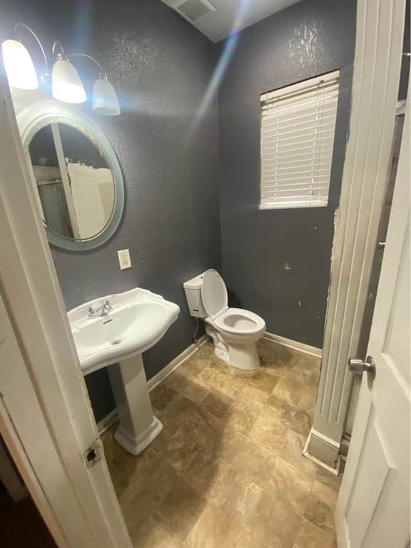 half bathroom with toilet, a textured wall, and baseboards