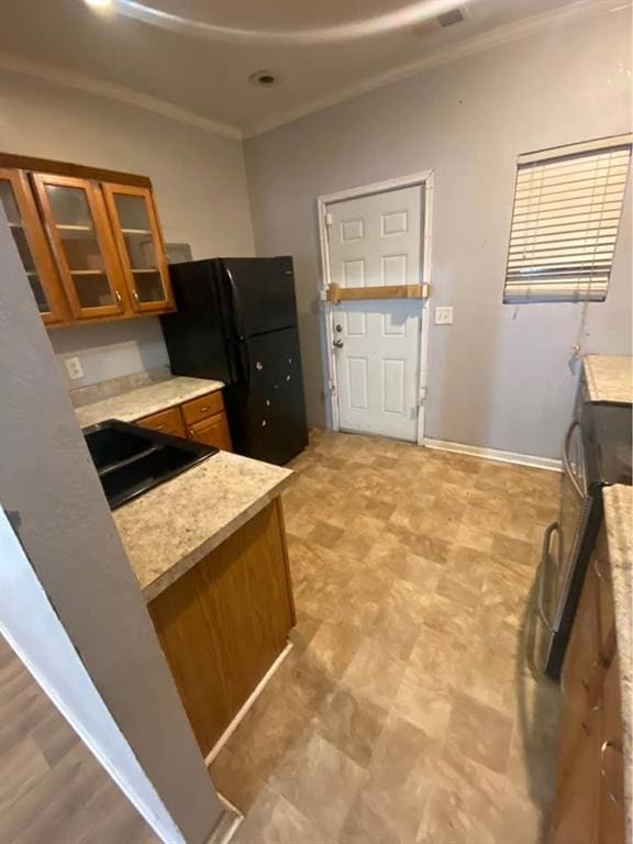 kitchen featuring brown cabinets, a sink, freestanding refrigerator, light countertops, and glass insert cabinets