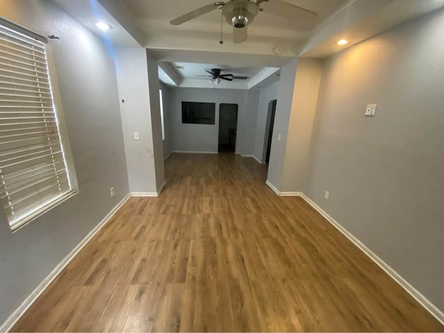 hallway with a tray ceiling, wood finished floors, baseboards, and arched walkways