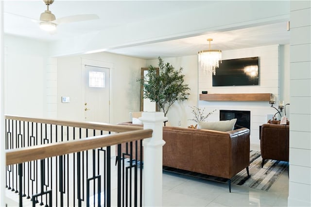 living room with light tile patterned floors, a glass covered fireplace, and ceiling fan with notable chandelier