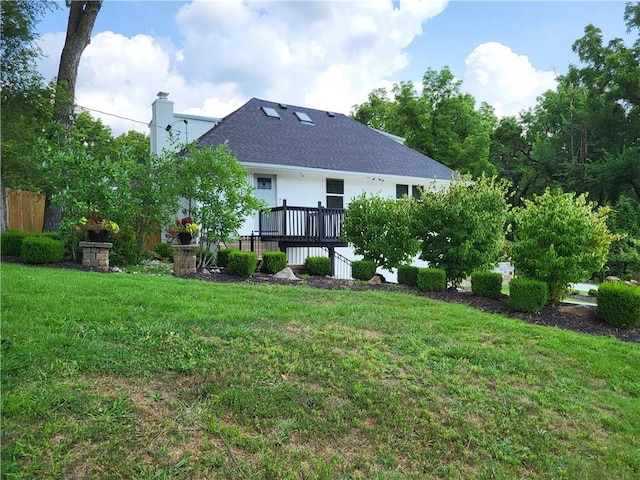 rear view of property featuring a deck, a yard, a chimney, and a shingled roof