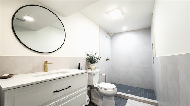 bathroom with vanity, a tile shower, wainscoting, tile walls, and toilet