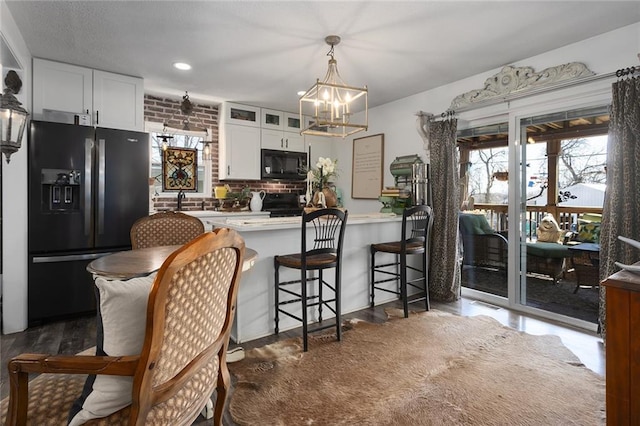 kitchen with black appliances, glass insert cabinets, white cabinetry, a kitchen breakfast bar, and a chandelier