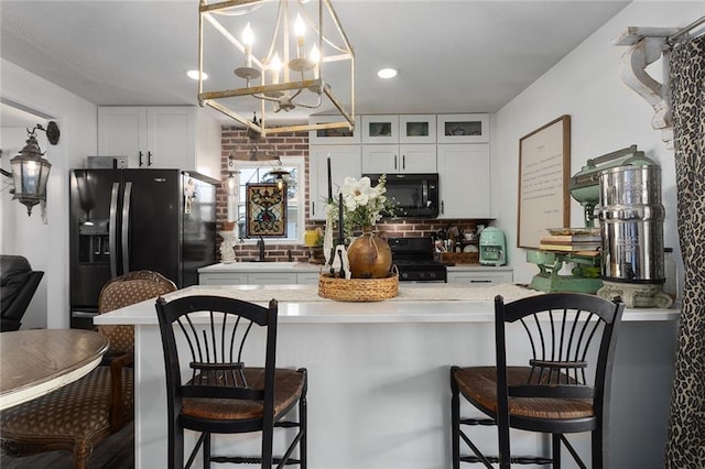 kitchen featuring a notable chandelier, black appliances, white cabinetry, light countertops, and glass insert cabinets