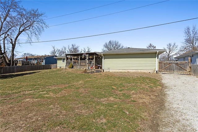 back of property with fence, a lawn, driveway, and a gate