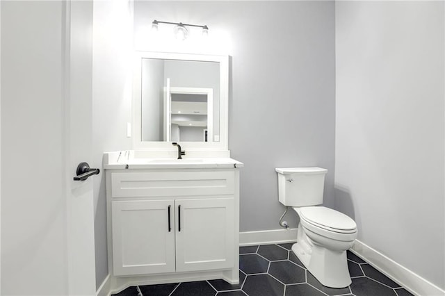half bathroom featuring toilet, vanity, baseboards, and tile patterned flooring