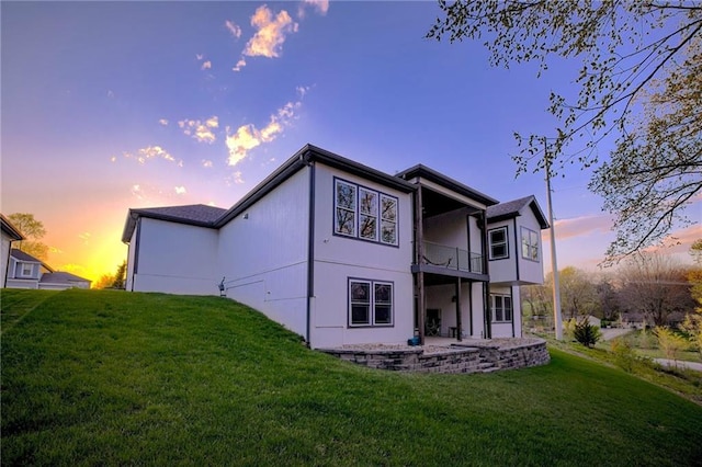 back of house at dusk featuring a patio area, stucco siding, a yard, and a balcony