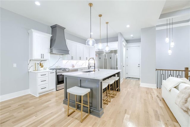 kitchen featuring a sink, a breakfast bar, stainless steel appliances, custom range hood, and light wood-style flooring