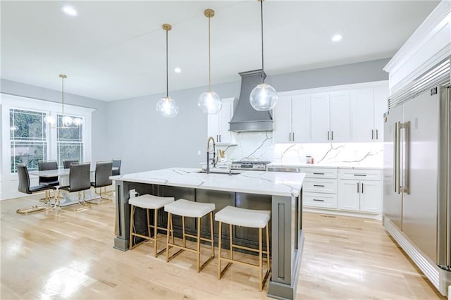 kitchen with built in refrigerator, premium range hood, decorative backsplash, and light wood finished floors