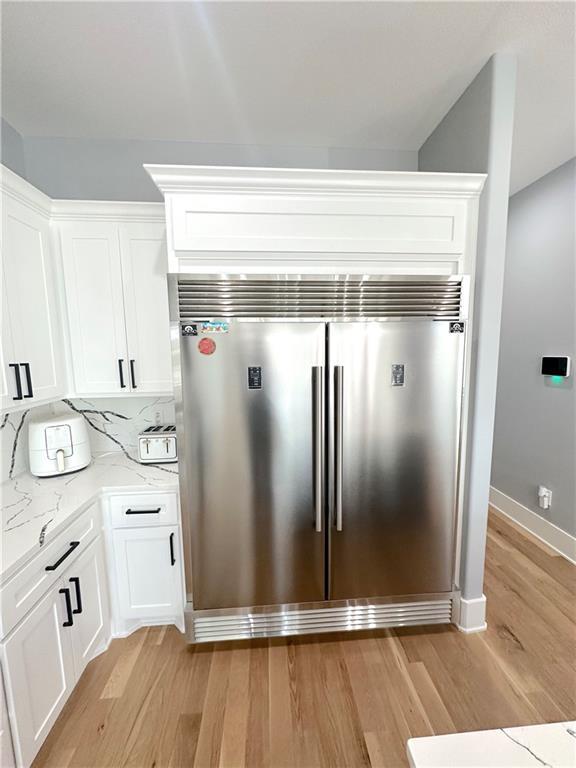 details with tasteful backsplash, built in refrigerator, white cabinets, light stone countertops, and light wood-style floors