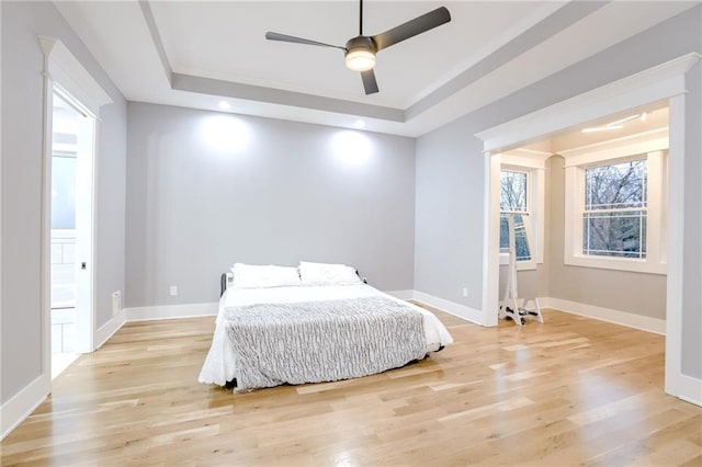 bedroom featuring light wood-type flooring, a raised ceiling, and baseboards