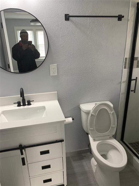 full bathroom with a textured wall, vanity, a shower stall, and toilet