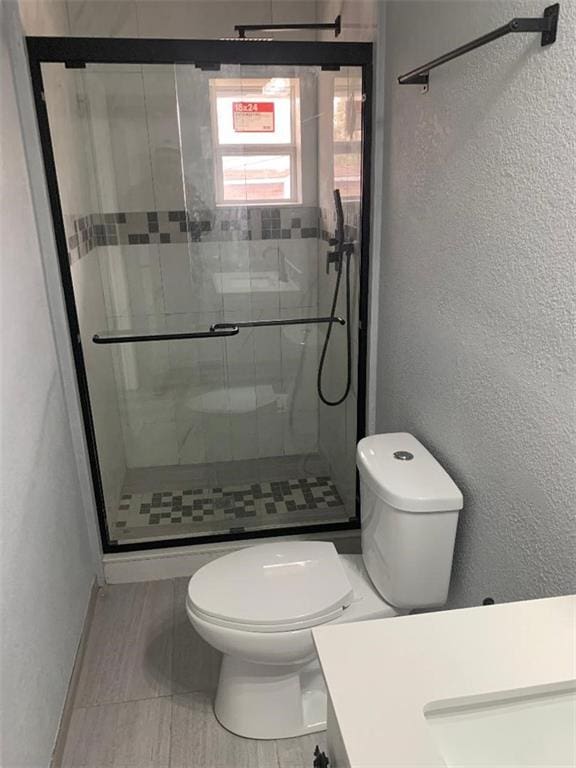 full bath featuring a shower stall, toilet, vanity, and a textured wall