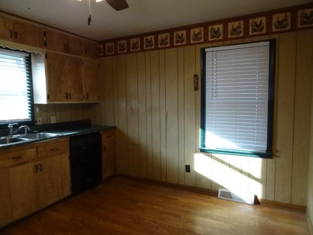 kitchen with visible vents, a sink, black dishwasher, dark countertops, and wood finished floors