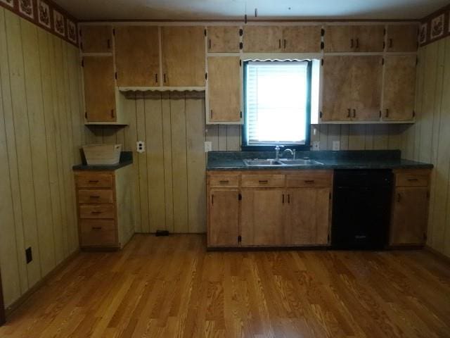 kitchen with a sink, light wood-style floors, black dishwasher, and dark countertops