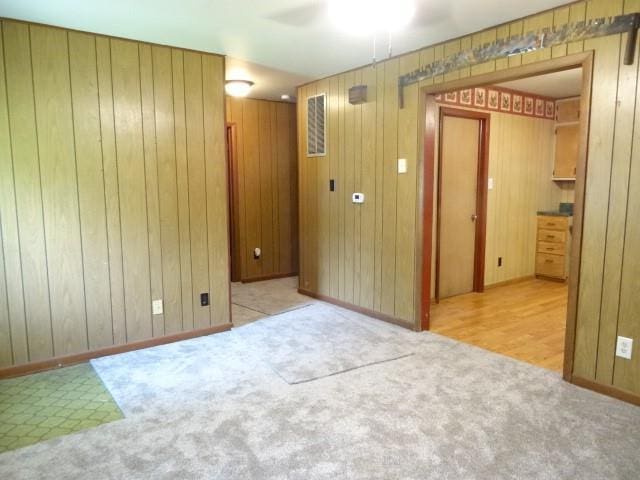 carpeted spare room with baseboards, wood walls, and a ceiling fan