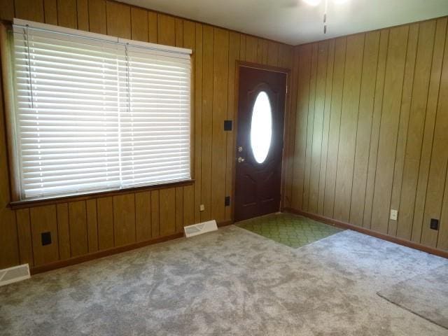 carpeted foyer featuring visible vents and wood walls